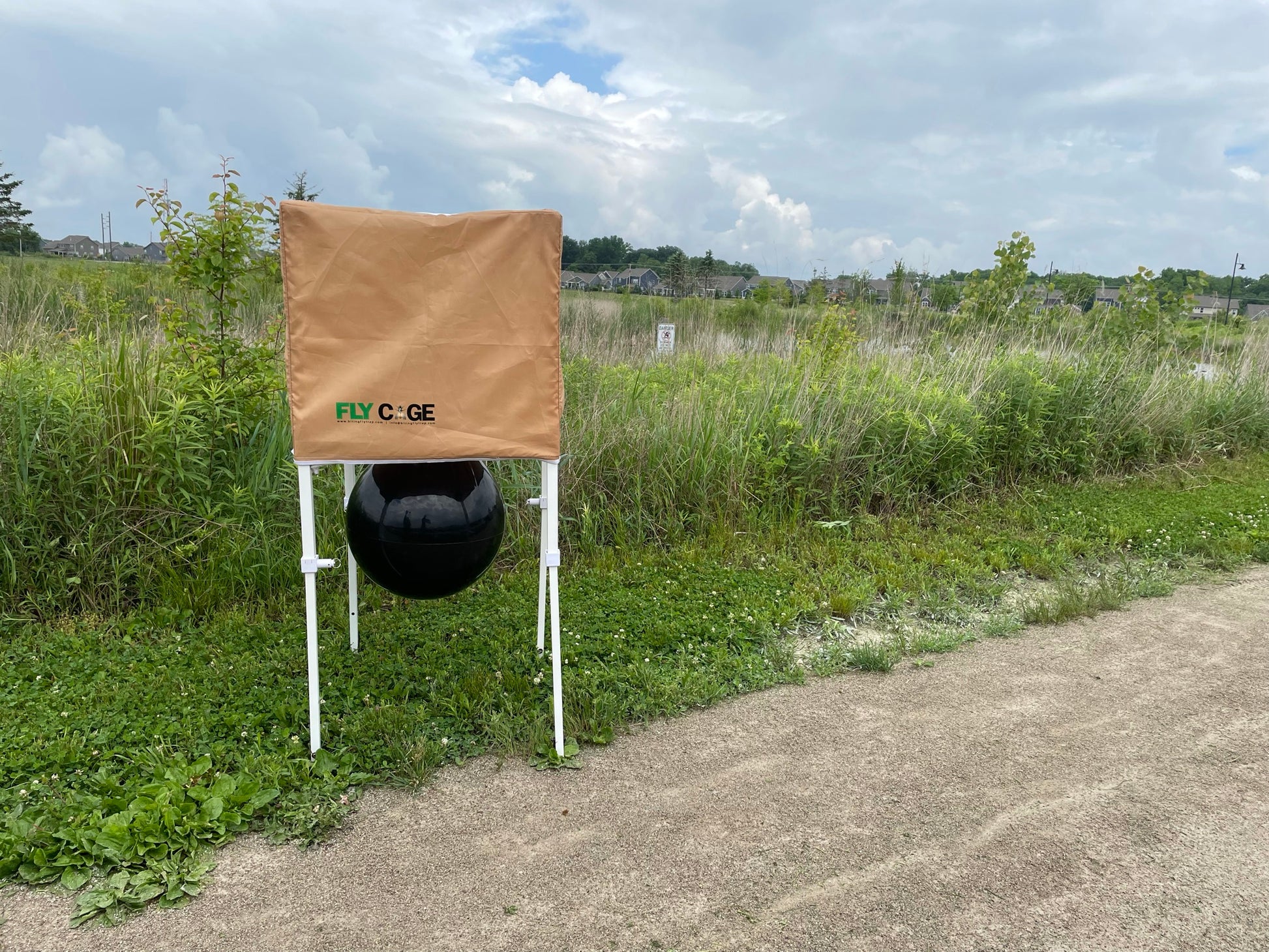 The Fly Cage chemical-free horse fly trap front view showing black attraction ball and tan catch cage in outdoor field setting